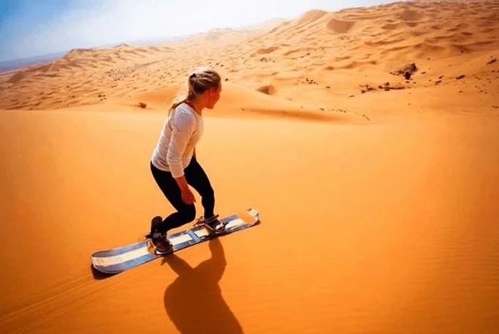 Touriste faisant du sandboard sur les dunes de Merzouga au coucher du soleil