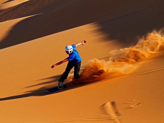 Vue panoramique sur un rider en sandboard descendant une grande dune à Merzouga