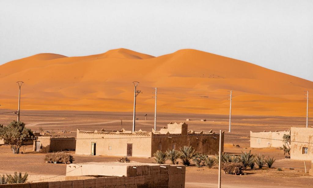 Riad Merzouga traditionnel avec architecture en pisé et vue panoramique sur les dunes dorées d'Erg Chebbi au coucher du soleil